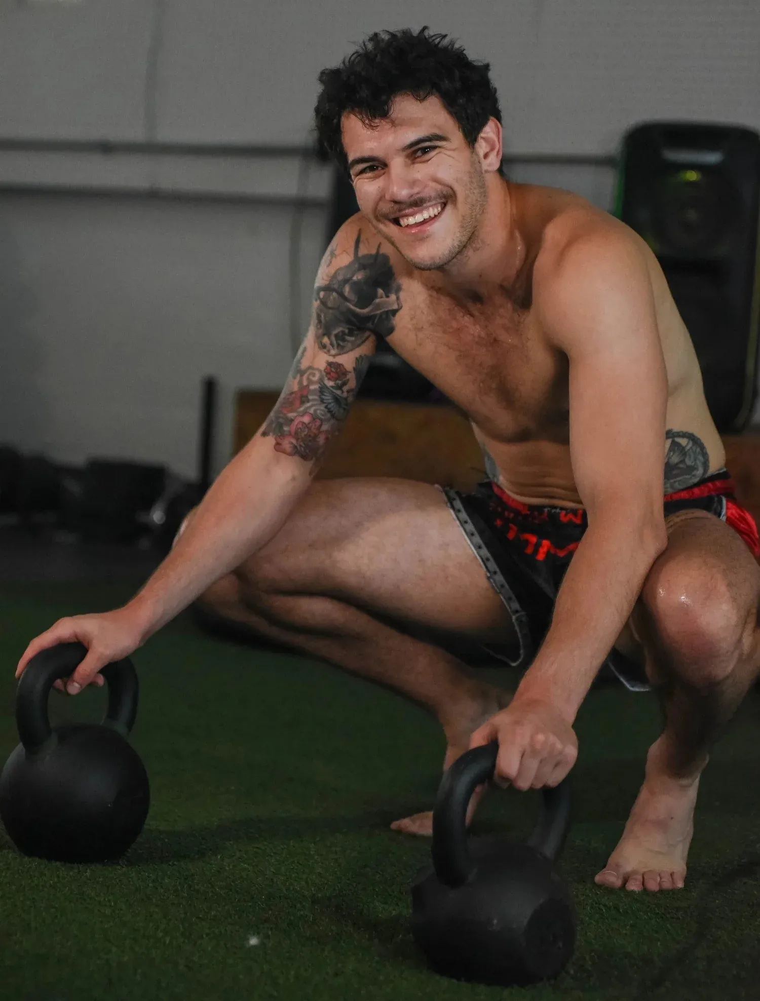 Coach Nico Aliaga smiling while resting his hands on two kettlebells